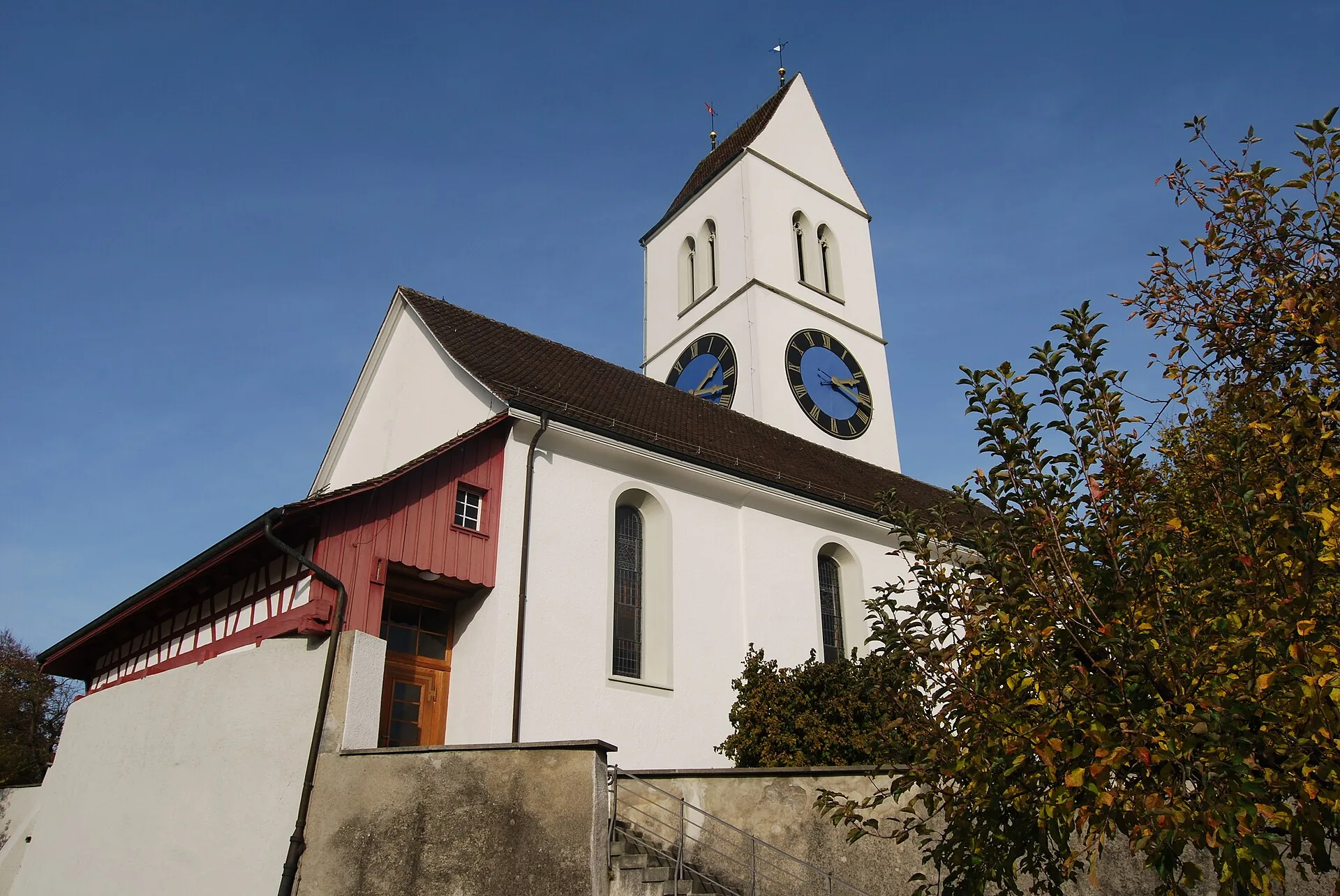 Reformierte Kirche Dinhard mit weissem Turm und Zifferblättern vor blauem Himmel