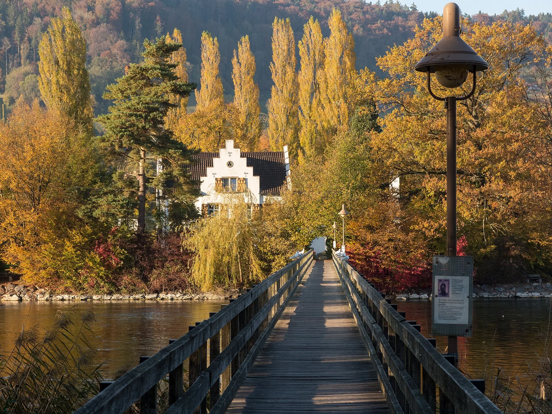 Holzsteg zur Insel Werd mit Klostergebäude zwischen herbstlichen Pappeln